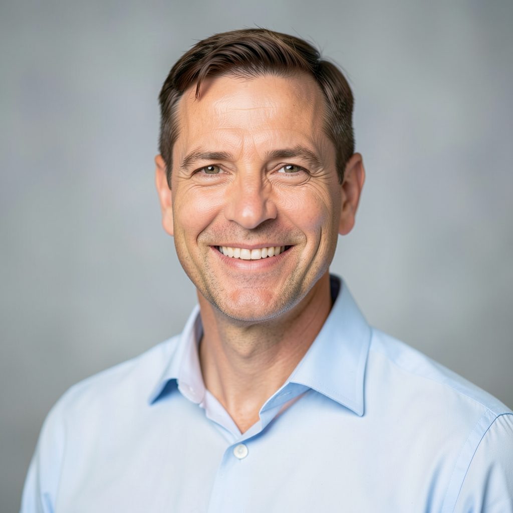 Portrait of a man in his forties with short brown hair and a warm smile, wearing a light blue shirt